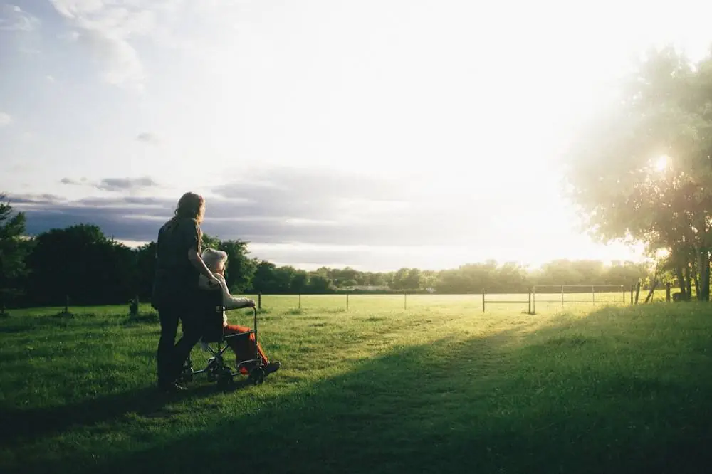 A person pushing a wheelchair across a field at sunset