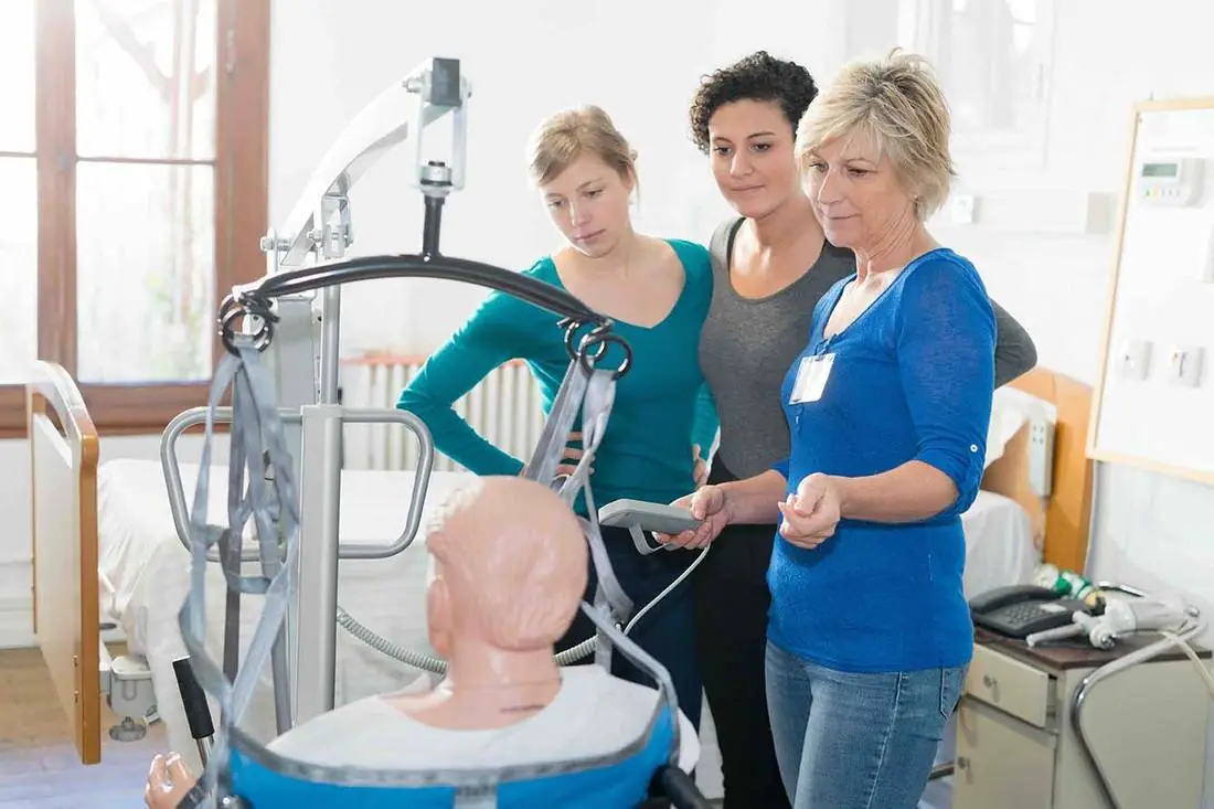 Three women practising moving and handling with a hoist in a training room