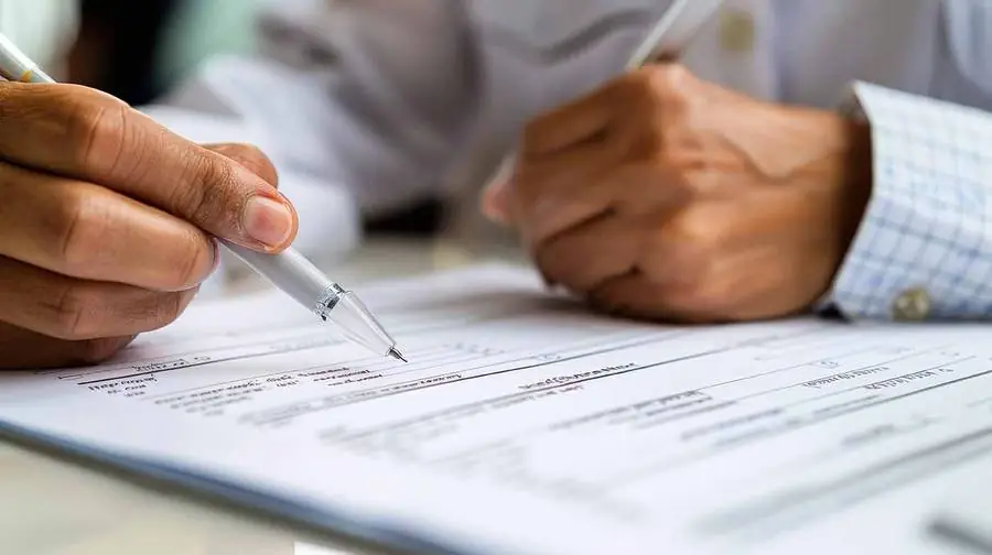 Hands completing a paper form at a table