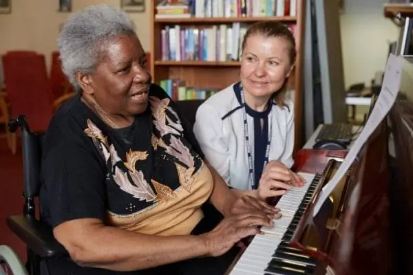 Older woman playing the piano with a carer beside her