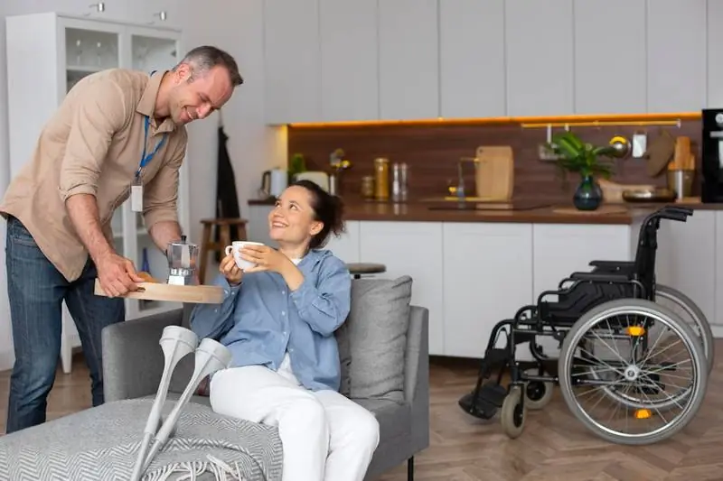 Carer helping an older man stand up from his sofa