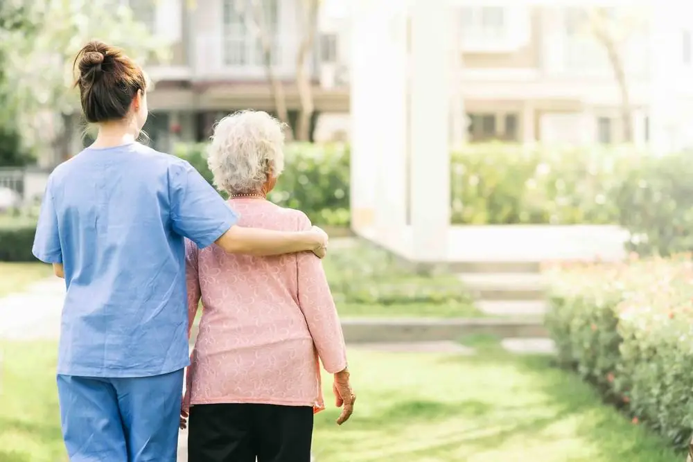 Carer and older woman walking arm in arm in a garden